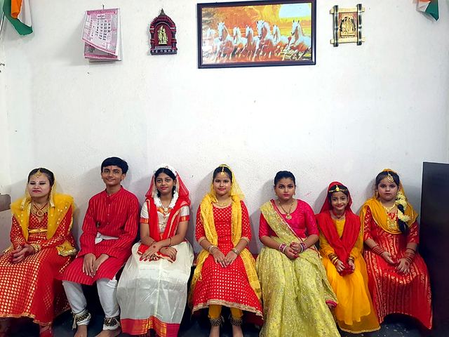 Women in red and yellow saris seated together before an event